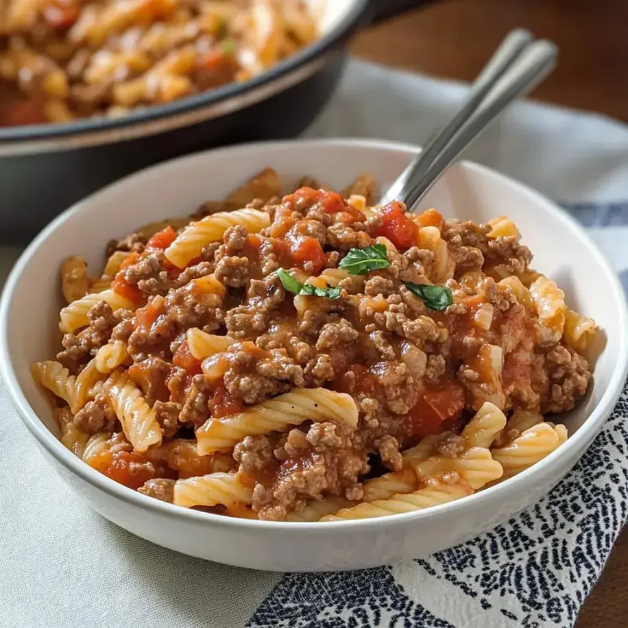 A dish of creamy pasta mixed with ground beef, topped with fresh basil.