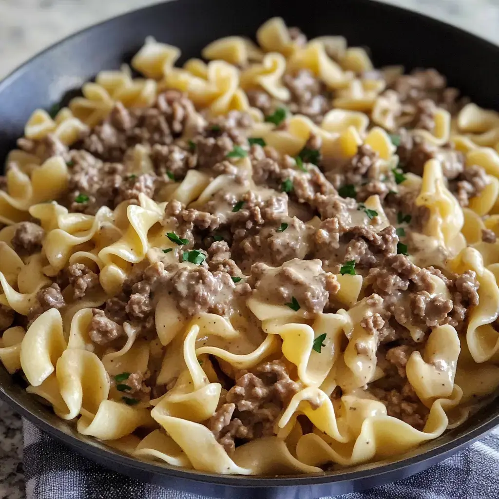 A skillet filled with noodles topped with saucy ground beef and sprinkled with parsley.