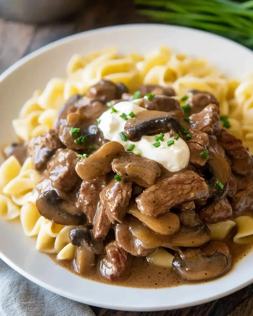 A dish of egg noodles topped with tender beef chunks, mushrooms, and a creamy dollop of sour cream, topped with freshly snipped chives.