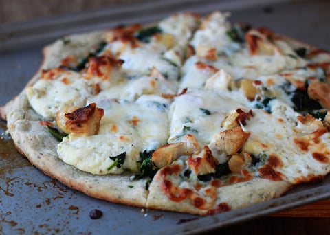 A pizza with chicken and broccoli on it.